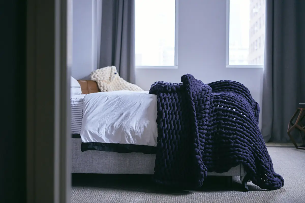 Quarto claro com um cobertor ponderado de tricô azul-marinho jogado sobre a cama