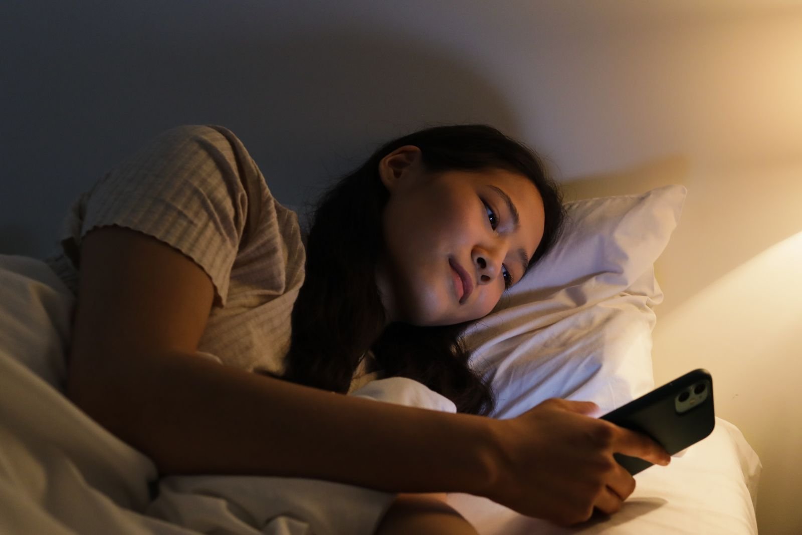 Mulher olhando o celular deitada na cama à noite, um dos erros que pioram a ansiedade na hora de dormir