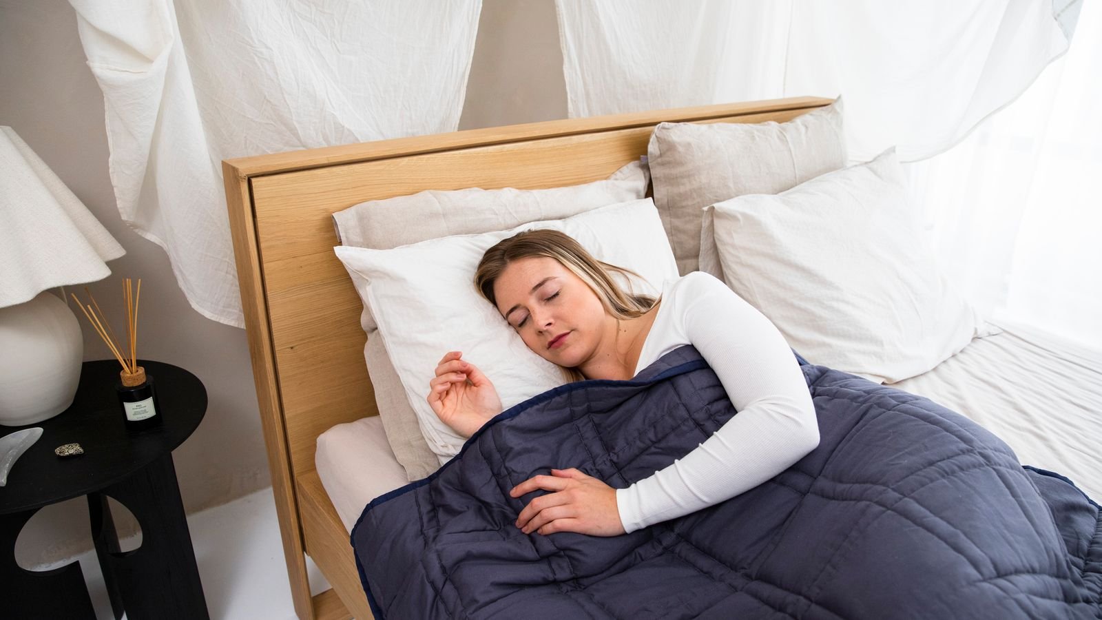 Mulher dormindo tranquila sob um cobertor ponderado azul, com o peso distribuído nos quadrados costurados